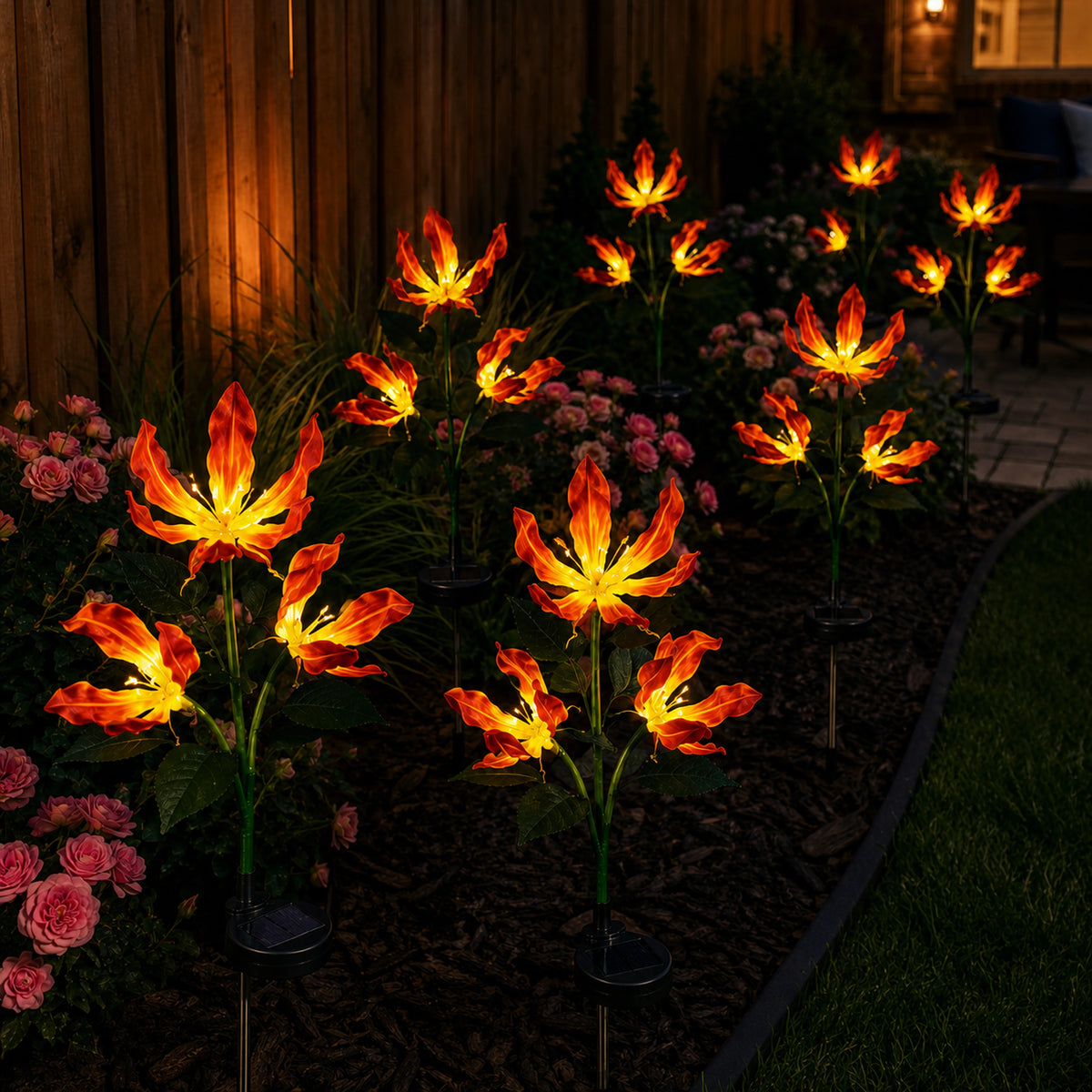 Solar fire lily garden lights glowing beside a flower bed at night