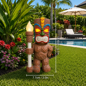 Solar tiki totem statue light holding a glowing torch beside tropical plants and a backyard pool